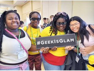 Four girls of color holding Geek is Glam sign at our STEM Expo Event for Girls